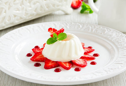 A white jelly-like dessert on top of sliced strawberries, topped with leaves