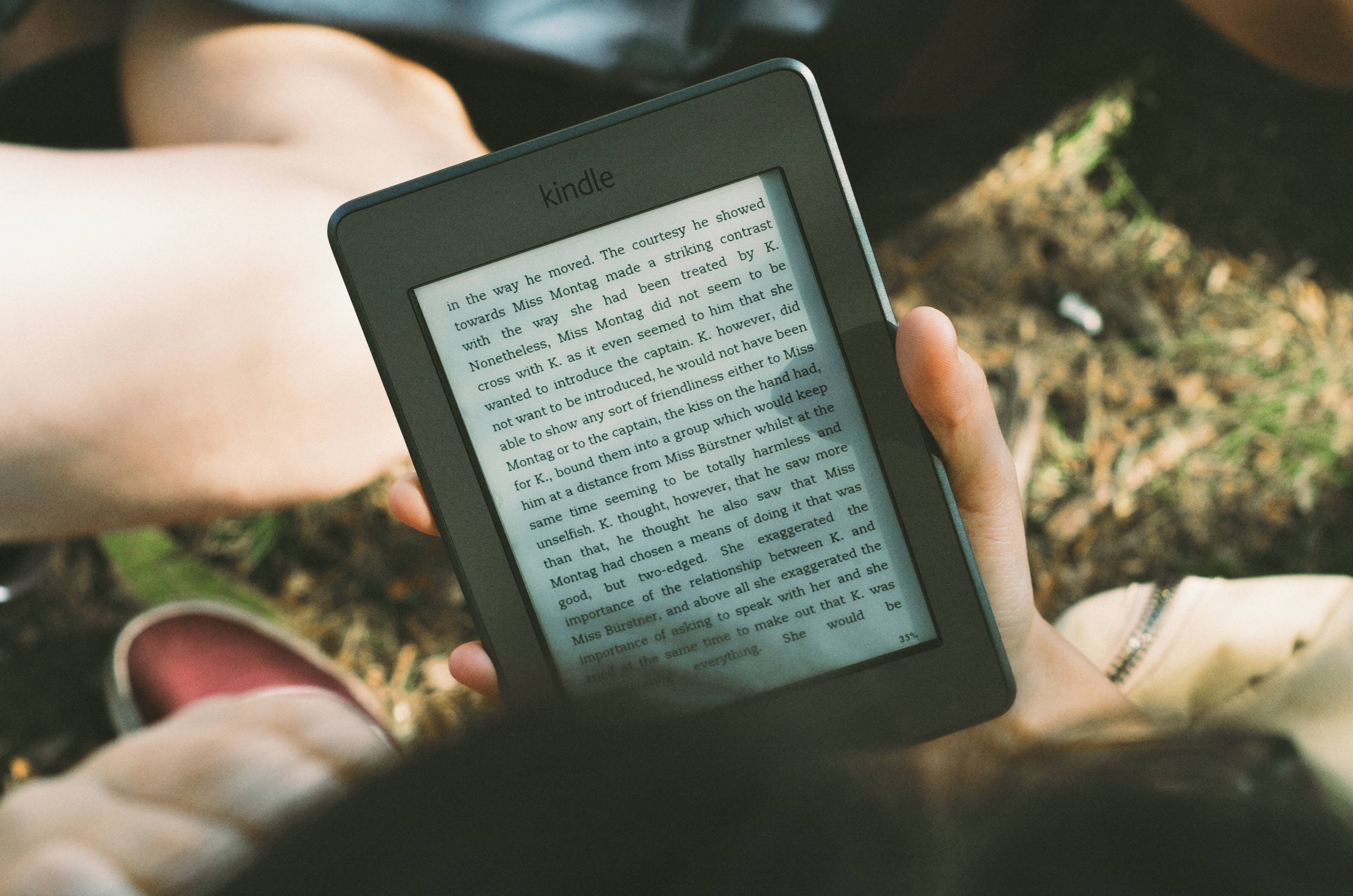 Hand holding a black Kindle, grass in the background