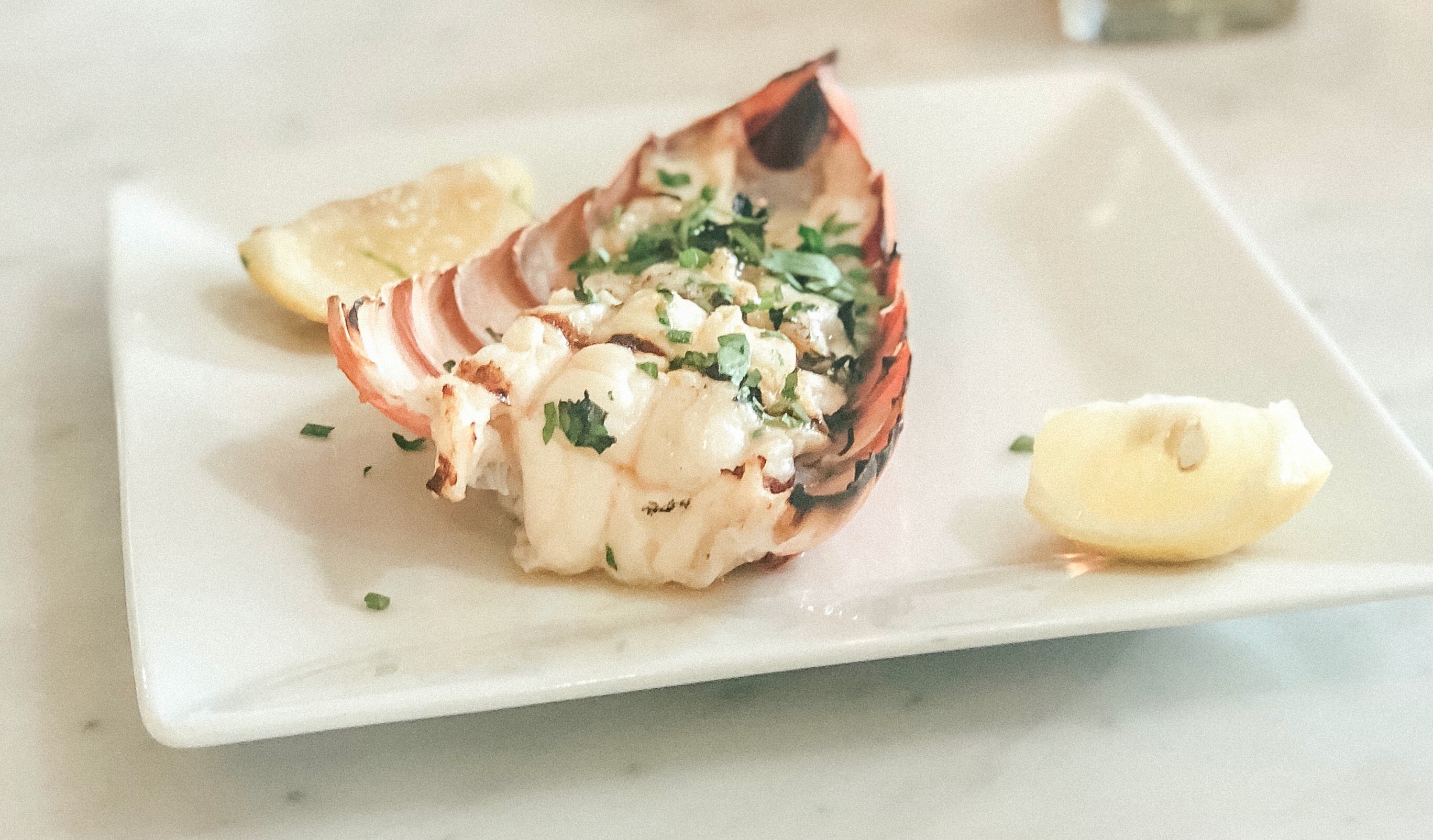 Lobster tail with lemons on herbs on a white plate