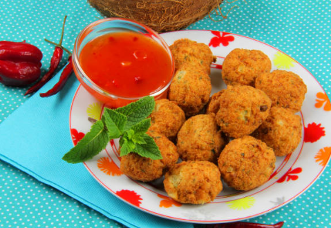 A plate of salt cod fritters (golden and round-shaped) with a side of spicy sauce